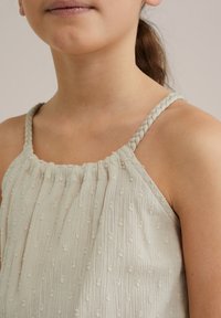 Svetlo bež majica z teksturirano tkanino, ki ima drobne vezenine. Pleteni naramnice in nagubano obdelavo ob izrezu.