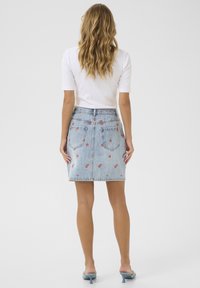 Jupe mini en denim avec un délavage bleu clair, ornée de broderies florales rouges. Design classique à cinq poches, ourlet effiloché et passants de ceinture.