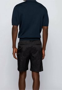 Tmavě modrá polo košile s krátkými rukávy a strukturovaným povrchem, doplněná o černé šortky s hladkou látkou a dvěma zadními kapsami.
