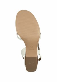 Vit klacksandals med en slät yta, justerbart ankelband och en texturerad beige gummisula med varumärket "Toms" präglat.