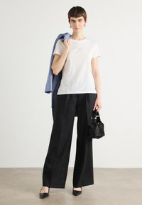 White cotton t-shirt with short sleeves, paired with loose black trousers, a light blue linen blazer draped over the shoulder, and a small black handbag.