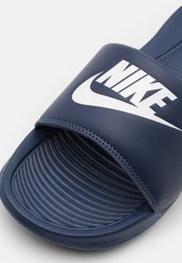 Sötétkék szandál, széles pánttal, fehér Nike logóval, texturált talprészel párhuzamos barázdákkal és sima élekkel.