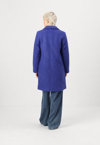 Purple textured coat with a collar, long sleeves, and mid-length design, paired with light blue wide-leg jeans. Back view displayed.
