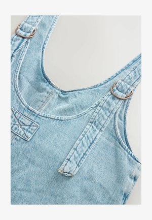 Svetlomodré denimové sedačky s nastaviteľnými popruhmi, kovovými krúžkami a prednou kapsou; textúrovaná látka s miernym vyblednutím a detailmi šitia.