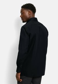 Zwarte langemouwen shirt met een button-down kraag, een gladde textuur en gestikte details op de manchetten, gezien van achteren.
