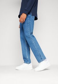 Jeans de mezclilla azul claro con corte recto, con un lavado deslavado. Combinados con zapatillas blancas y una camisa de manga larga azul marino.