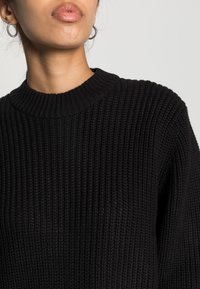 Schwarzer gestrickter Pullover mit gerippter Textur, Rundhalsausschnitt und langen Ärmeln, der eine enge Passform und subtile Details zeigt.