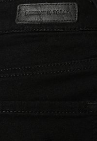 Tissu en denim noir avec une étiquette en cuir portant le texte « SOMEDAY IS TODAY ». Détails de couture visibles le long des coutures.