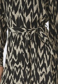 Μαύρο και μπεζ φόρεμα με σχέδιο, που διαθέτει σχέδιο ikat, κουμπιά μπροστά, μακριά μανίκια και ζώνη που δένει στη μέση.