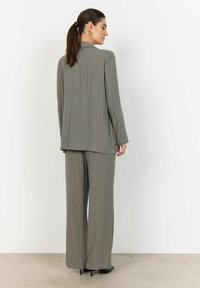 Šedý oblek s vertikálnymi pruhmi, ktorý má dlhý blazer a široké nohavice. Tkanina vyzerá textúrovane, s priliehavým strihom a jemnými kontrastnými prúžkami.