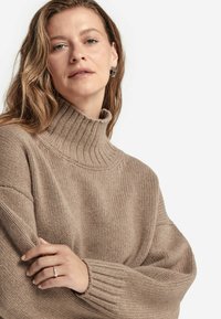 Beige gestrickter Rollkragenpullover mit gerippten Bündchen, weitem Schnitt und weicher Textur, entworfen für Wärme und Komfort.