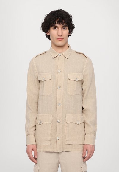 Béžová košile-jacket z lnu s dlouhými rukávy, s knoflíkovým zapínáním a čtyřmi kapsami s klopami. Obsahuje ramenní epolety a texturovanou látku.