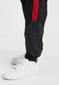 Svart och röd atletisk joggers har en mönstrad svart panel med små vita prickar, kombinerade med vita Nike-sneakers.