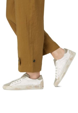 Weiße Sneaker mit beigen Wildlederelementen, durchbrochener Seitenverarbeitung und einer weichen, strukturierten Sohle. Getragen zu lockeren braunen Hosen.