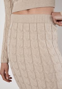 Beiger Strickrock mit einem gemusterten Textur aus ineinandergreifenden Ovalen und geripptem Bund. Nahaufnahme, die die Weichheit des Stoffes betont.