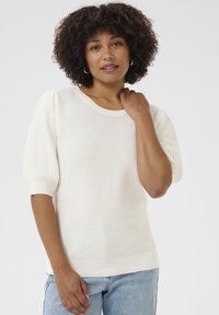 Pullover di maglia color crema con scollatura rotonda, maniche a sbuffo corte, polsini e orlo a coste. Indossato sopra un paio di jeans in denim blu.