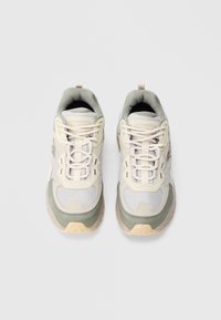 Ténis com parte superior em malha e sintético em tons de creme e verde claro. Apresenta fecho com atacadores e colarinho almofadado. Sola em borracha.