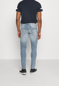 Jeans ajustados de color azul claro con un lavado desgastado, cinco bolsillos y sutiles detalles de costura, combinados con una camiseta azul marino y zapatillas negras.