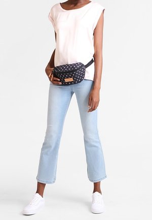 Person iført en hvid ærmeløs top, lyseblå cropped jeans, hvide sneakers og en sort polkaprik-bæltetaske med læderlogo.