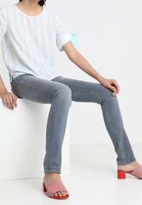 Top a rayas en azul claro y blanco con mangas cortas que presenta acentos de lazo, combinado con unos jeans gris entallados y sandalias de dedo rosas.