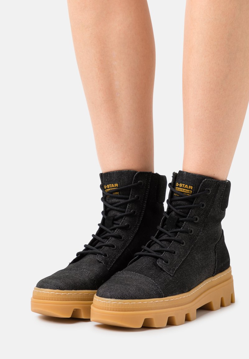 Bottes montantes noires en tissu texturé avec semelles en caoutchouc ; elles présentent de grosses lacets, un col rembourré et une semelle de couleur gomme contrastante.
