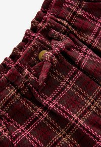 Pantaloni a quadri bordeaux realizzati in tessuto testurizzato. Presentano una vita con cinturino annodato, un bottone dorato e linee in rosa e beige in contrasto nel motivo.