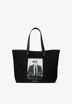 Borsa a spalla nera in tessuto, con una stampa fotografica bianca di un uomo con occhiali da sole, dotata di manici in pelle nera e testo sotto l'immagine.