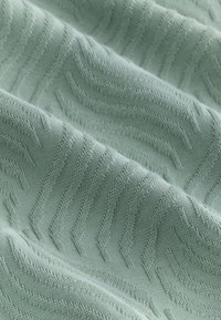 Tissu vert clair doux avec un motif zigzag en relief et texturé et des plis subtils créant une surface ondulée.