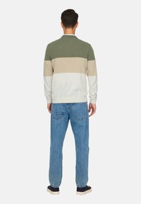 Pull pour homme à rayures vertes, beiges et blanches. Tissu en maille douce, col rond, poignets et ourlet côtelés. Porté avec un jean denim bleu ample.