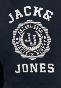 Sudadera de color navy con un logo circular blanco que incluye "JACK & JONES", "ESTABLECIDO" y "MIL NOVECIENTOS NOVENTA", decorado con acentos de laurel.