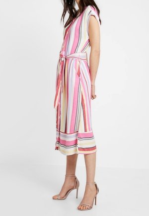 Femme portant une robe sans manches, longueur genou, à rayures verticales roses, blanches et jaunes, nouée à la taille, associée à des sandales à talons hauts couleur nude.