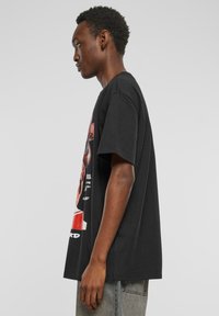 Svart bomull T-skjorte med en stor fargerik grafikktrykk på fronten, korte ermer og en løs passform, kombinert med grå jeans.