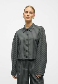 Taillierte Jacke aus dunkelgrauem Stoff mit vertikalen weißen Streifen. Sie verfügt über einen klassischen Kragen und weite Ärmel, kombiniert mit passenden Hosen.