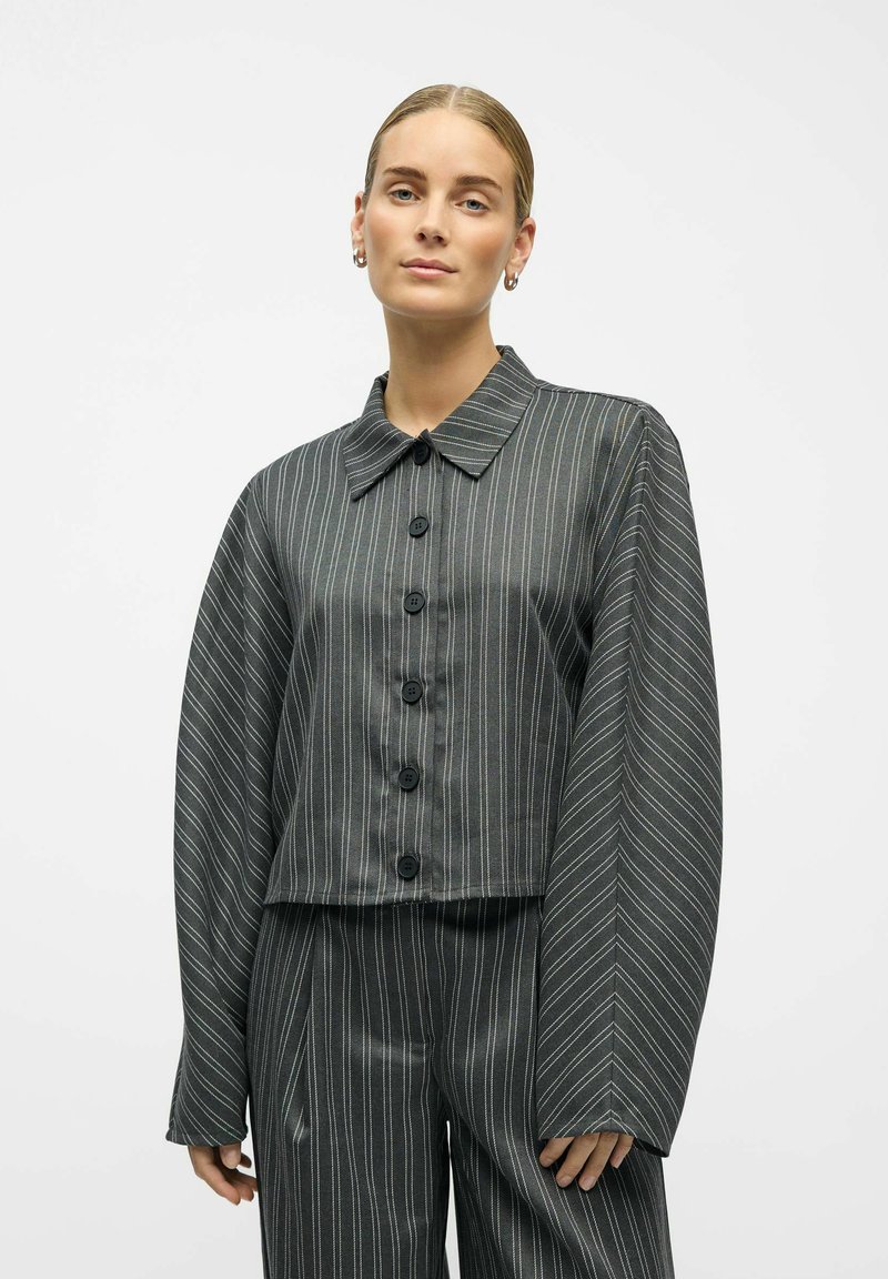 Taillierte Jacke aus dunkelgrauem Stoff mit vertikalen weißen Streifen. Sie verfügt über einen klassischen Kragen und weite Ärmel, kombiniert mit passenden Hosen.
