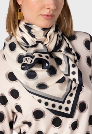 Foulard en soie avec un fond crème orné de motifs circulaires noirs et gris, et une bordure accentuée. Noué autour du cou et d'une texture douce.