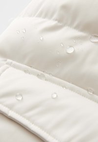 Waterdichte crème pufferjack fabric met verticale stiksels. Kleine waterdruppels parelen op het oppervlak en benadrukken de impermeabiliteit ervan.