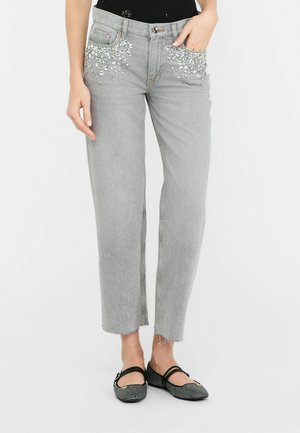 Jeans in denim grigio con tasche decorate da strass trasparenti, vestibilità a gamba dritta, orlo strappato e un lavaggio chiaro. Indossate scarpe nere basse.