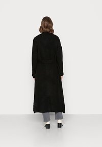 Czarny dzianinowy długi kardigan z paskiem w talii, z teksturowanym wzorem, szerokimi rękawami i luźnym krojem, zestawiony z szarymi dżinsami i szpilkami.