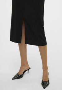 Černá kordurová midi sukně s předním rozparkem, doplněná lesklými černými lodičkami s špičatou špičkou. Viditelné jsou hladké textury a čisté linie.