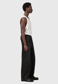Schwarze weite Jeans mit hoher Taille, kombiniert mit einem gestreiften weißen Tanktop. Besitzt eine flache Vorderseite und seitliche Taschen, mit einer glatten Textur.