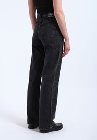 Black denim jeans with a high waist, wide-leg cut, and visible stitching. Features two back pockets and a logo patch on the waistband.