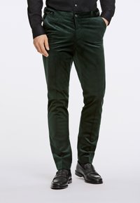 Pantaloni in velluto verde scuro con una vestibilità slim, caratterizzati da una superficie liscia, due tasche laterali e due bottoni decorativi in vita.