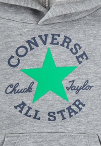 Siv hoodie z velikim zelenim zvezdnim motivom. Besedilo pravi "CONVERSE ALL STAR" in "Chuck Taylor" v temno modrem fontu. Mehka tekstura.