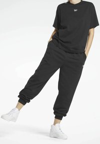 Svart bomulls T-shirt med kort ärm och rund halsringning, tillsammans med svarta joggers med mudd vid anklarna och sidofickor. Vita sneakers.