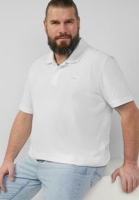 Witte polo met kraag en korte mouwen, met een subtiele s.Oliver-logo op de borst. G gedragen met lichtblauwe jeans.