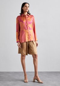 Silk skjorte i rosa og oransje abstrakt mønster, kombinert med beige satengshorts og beige blokkhæl sandaler. Jevn tekstur gjennom hele.