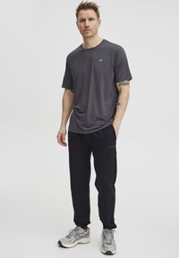 Donkergrijze sportt-shirt met ronde hals, gecombineerd met zwarte trainingsbroek en grijze sneakers, met logo detail op de kleding.