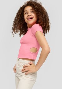 Różowy prążkowany crop top z krótkim rękawem i wycięciami, w zestawie z jasnobeżowymi dopasowanymi spodniami, podkreślającymi zgrabny, nowoczesny krój.