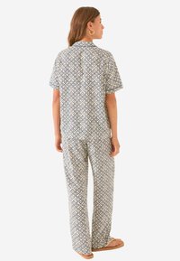 Patroon pyjama set in crème met marineblauwe krullen, short-sleeve shirt, loszittende broek, lichtgewicht stof en platte sandalen.