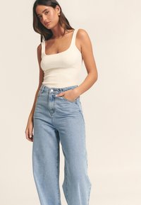 Balts ribots tank tops ar kvadrātveida izgriezumu, kombinēts ar gaiši zilām, augsta vidukļa plaša stila džinsu biksēm, kurām ir priekšējās kabatas un pogu aizdare.